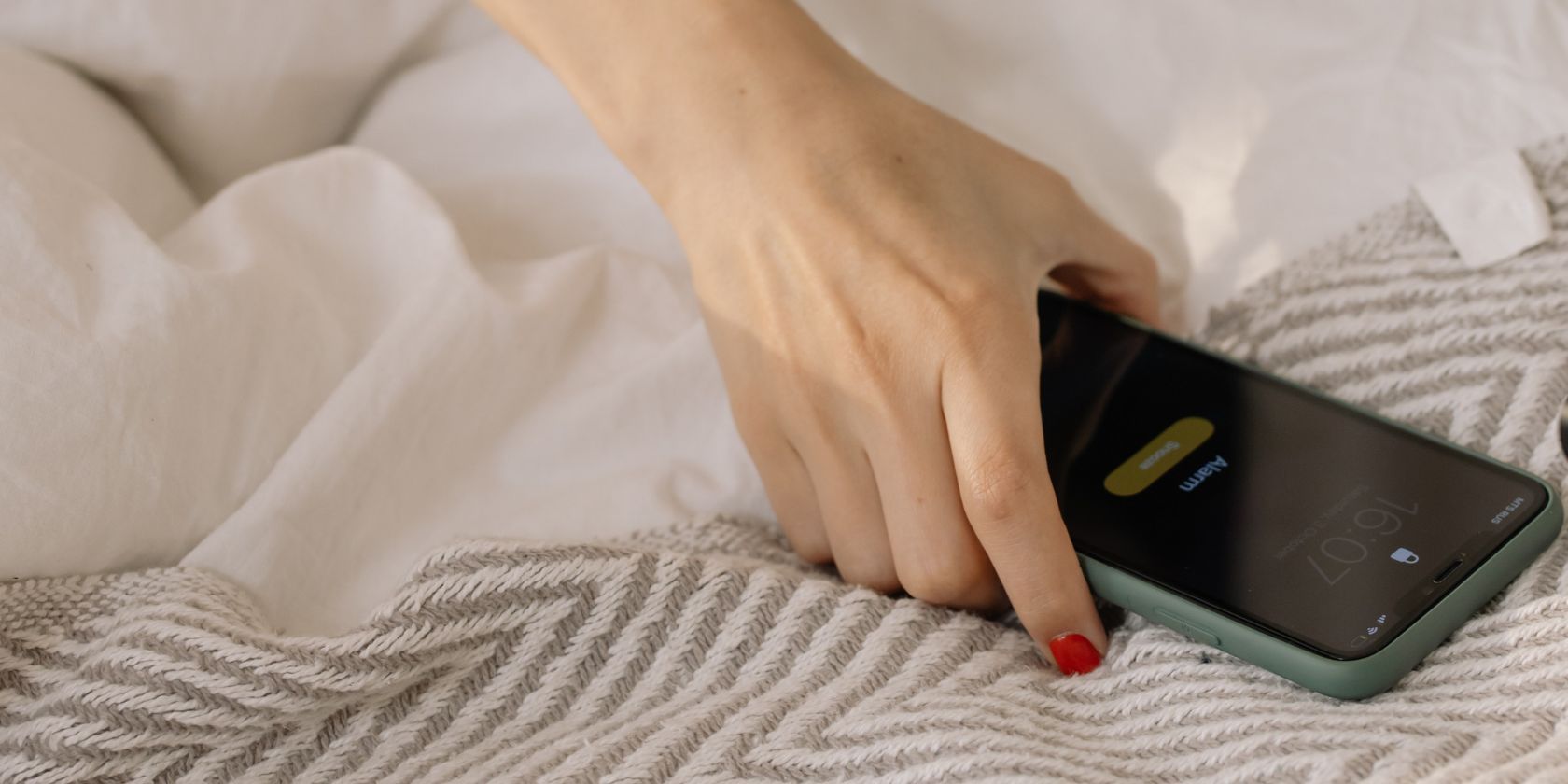 Mulher na cama chegando para desligar o alarme do smartphone
