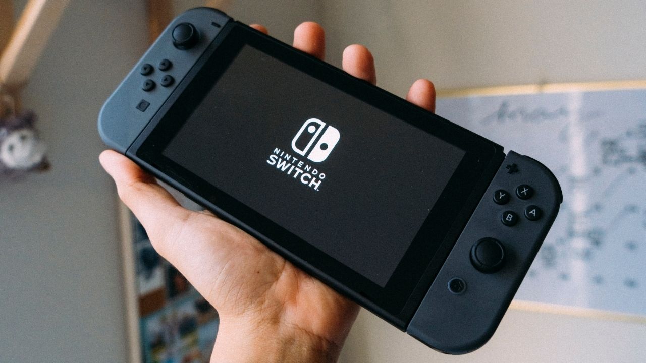Uma fotografia de um Nintendo Switch com Joy Cons cinza sendo segurado no ar 